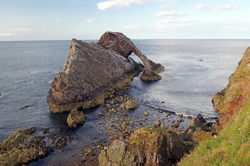 Rocky island by the sea with gentle waves surrounded by a clear sky, Bow Fiddle Rock, Aberdeenshire, Buckie, Scotland, United Kingdom
