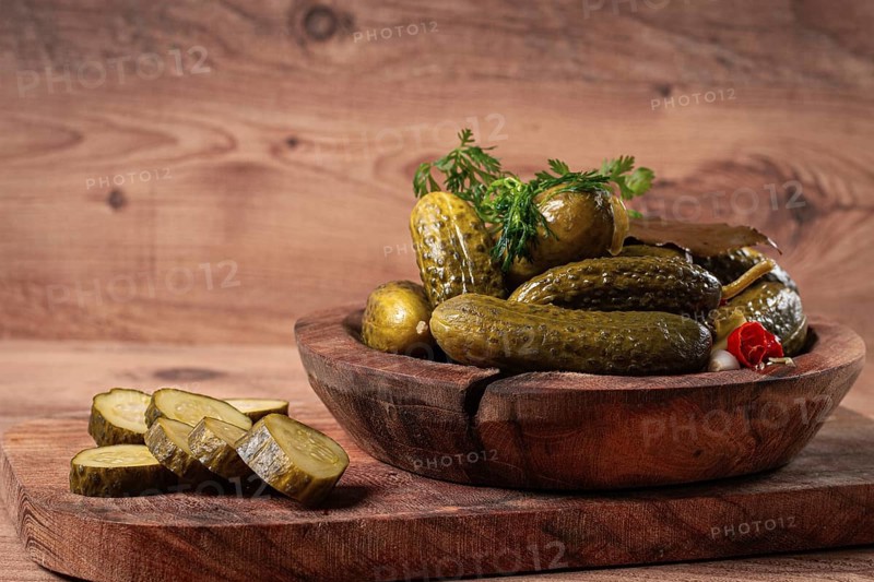 Pickled cucumbers in a wooden bowl with herbs and spices, close-up, rustic style