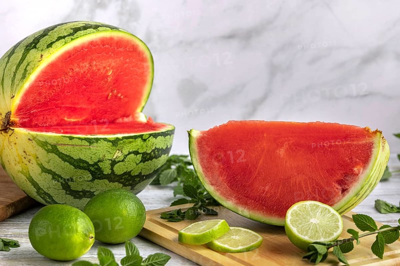 Sliced watermelon with limes and mint leaves on a wooden board