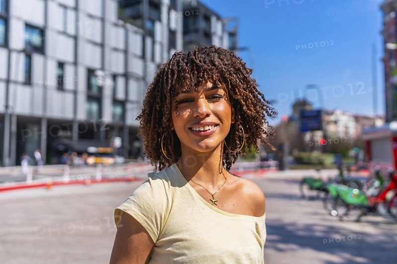 Smiling young woman enjoying a sunny summer day in a vibrant urban setting, surrounded by modern architecture and cheerful energy