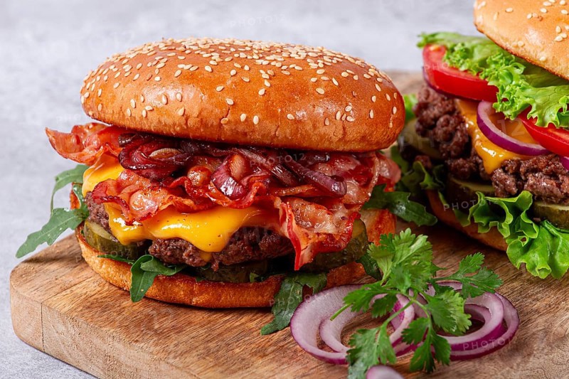 Two burgers with beef patty, fried bacon, cheddar cheese, tomatoes, homemade, no people
