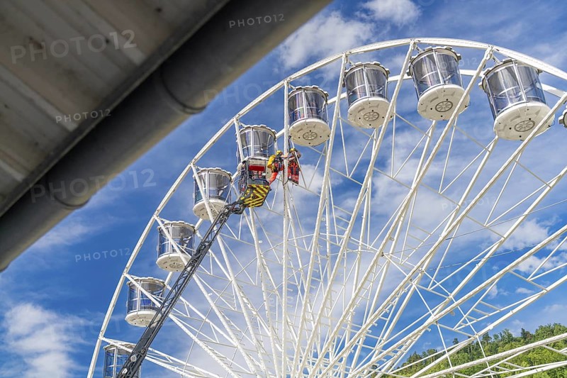 A crane lifts people on a large Ferris wheel up into the blue sky, fire brigade exercise for gondola rescue, Germany