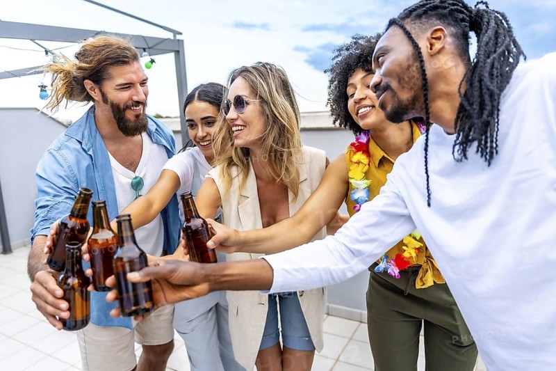 Happy friends celebrating on a rooftop, toasting with beer bottles and enjoying quality time together in a vibrant summer atmosphere