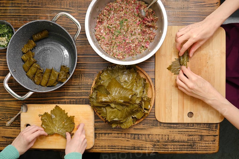 Overhead view of hands making dolma using vine leaves and a ground meat on a kitchen table