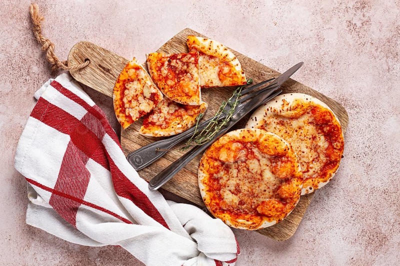 Four pizzetta Margaritas, on a cutting board, on a light gray surface, top view