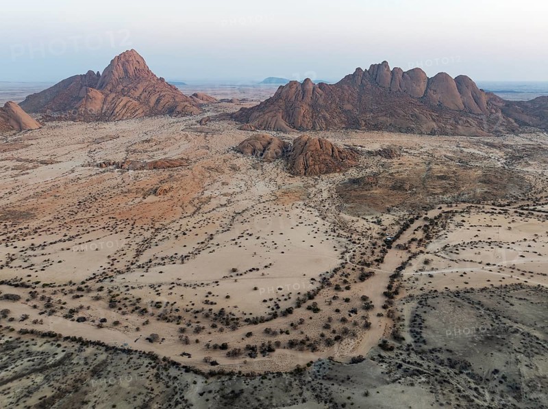 Spitzkoppe (1728 m) - on the left - and Pondok Mountain majestically rise above the surrounding desert plains. At dawn. Aerial view. Drone shot. Damaraland, Namibia