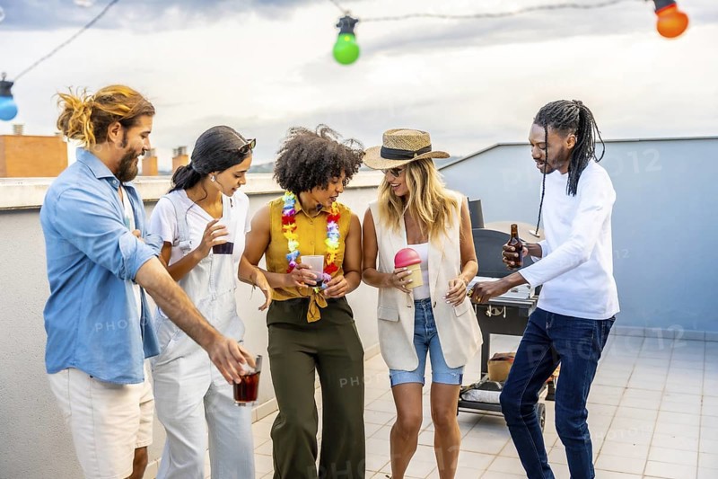 Cheerful group of diverse friends enjoying drinks, dancing, and socializing at a rooftop barbecue party