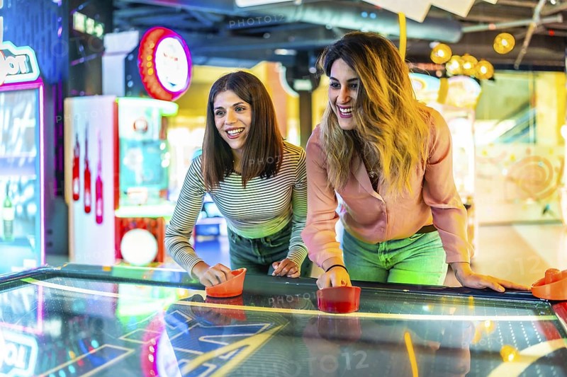 Two young women enjoying a friendly game of air hockey in a vibrant arcade, showcasing fun and entertainment