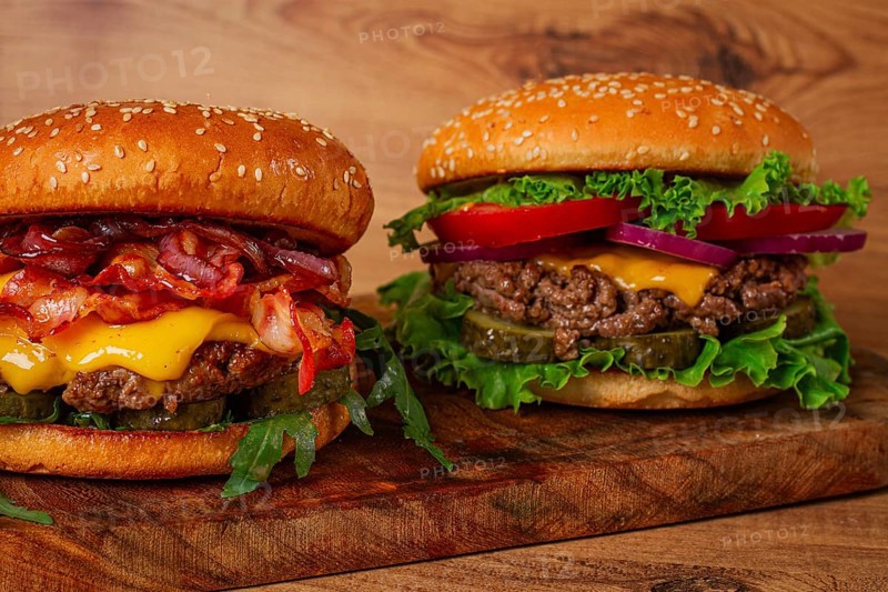 Two burgers with beef patty, fried bacon, cheddar cheese, tomatoes, homemade, no people