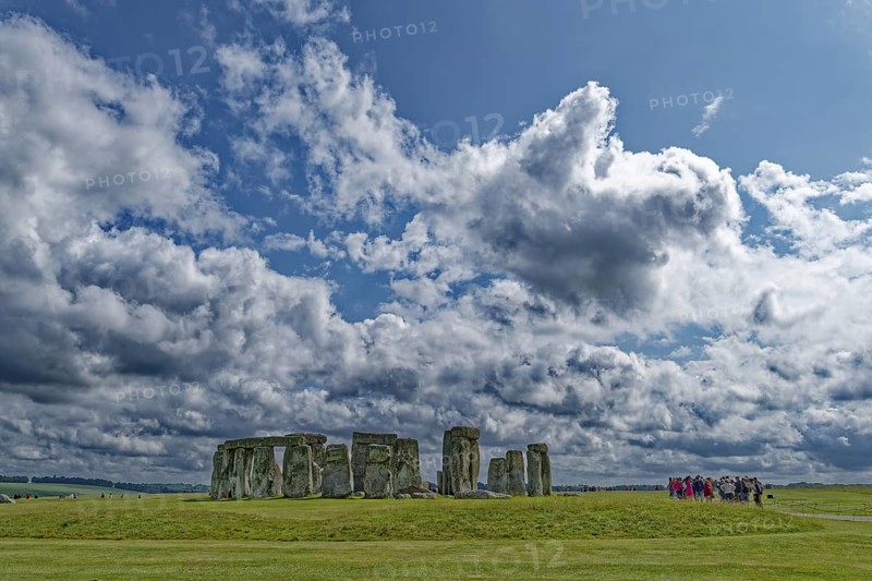 A group of tourists visits Stonehenge. The stone circle, a National Trust, UNESCO World Heritage Site, is a megalithic structure from the Neolithic period and is considered a place of power. The site consists of a ring-shaped earth wall, inside which there are various formations of carved stones grouped around the centre. Amesbury, Wiltshire, South England, Great Britain