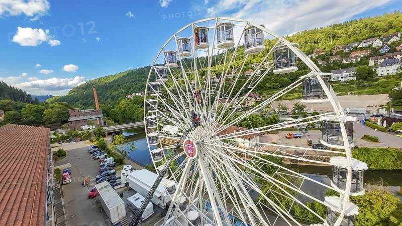 A Ferris wheel with lorries underneath, near a river in a green environment, fire brigade exercise for gondola rescue, Germany