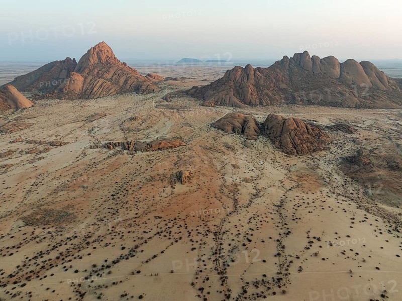 Spitzkoppe (1728 m) - on the left - and Pondok Mountain majestically rise above the surrounding desert plains. At dawn. Aerial view. Drone shot. Damaraland, Namibia