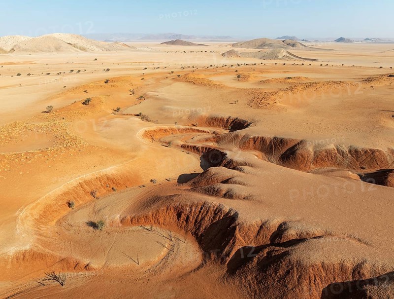 Canyons, arid plains grown with camelthorn trees (Vachellia erioloba) and isolated mountain ridges in the Tsondab Valley in the Namib Desert. Aerial view. Drone shot. Namibia
