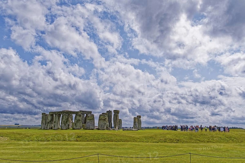 A group of tourists visits Stonehenge. The stone circle, a National Trust, UNESCO World Heritage Site, is a megalithic structure from the Neolithic period and is considered a place of power. The site consists of a ring-shaped earth wall, inside which there are various formations of carved stones grouped around the centre. Amesbury, Wiltshire, South England, Great Britain