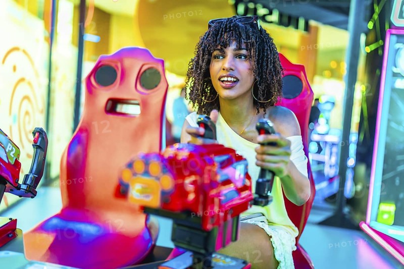 Young woman enjoying an exciting moment while playing a vibrant car racing arcade game in a bustling shopping mall