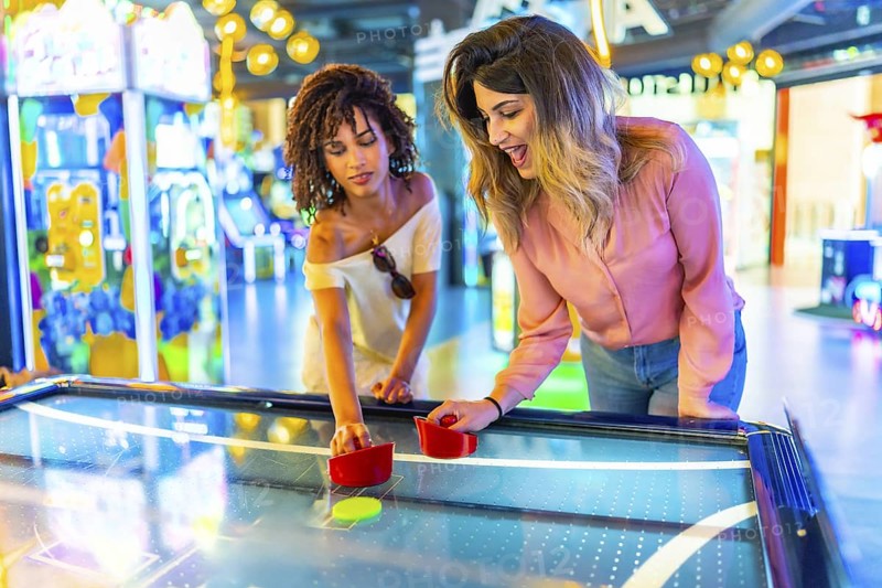 Two young women enjoying a friendly game of air hockey in a vibrant arcade, showcasing the fun and excitement of indoor entertainment