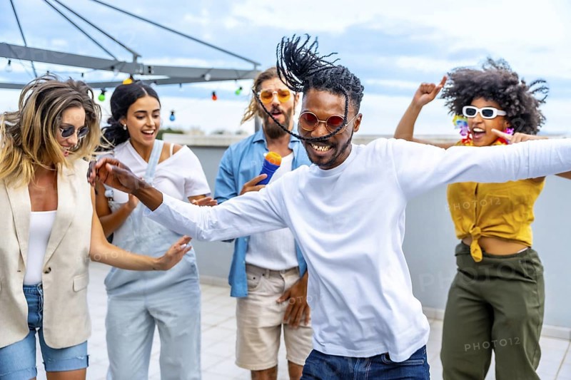 Young people dancing and singing joyfully at a vibrant rooftop party, enjoying music and celebrating summer together with friends