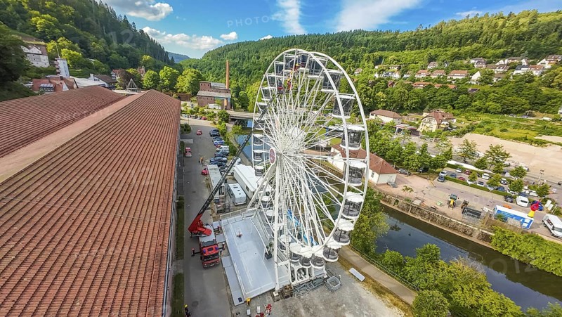 View of a Ferris wheel in a wooded environment with red roofs and blue sky, fire brigade exercise for gondola rescue, Germany