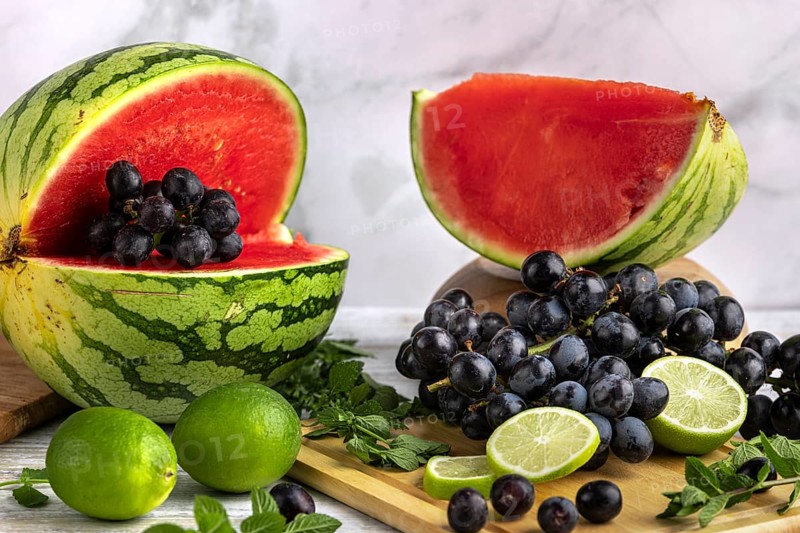 Sliced watermelon, grapes and limes on a wooden board with mint leaves