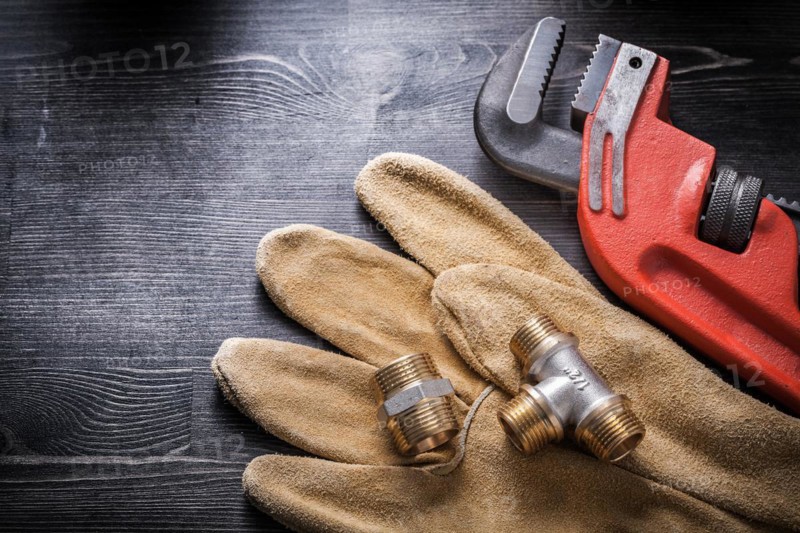 Pipe wrench plumbing fittings safety gloves on wooden board