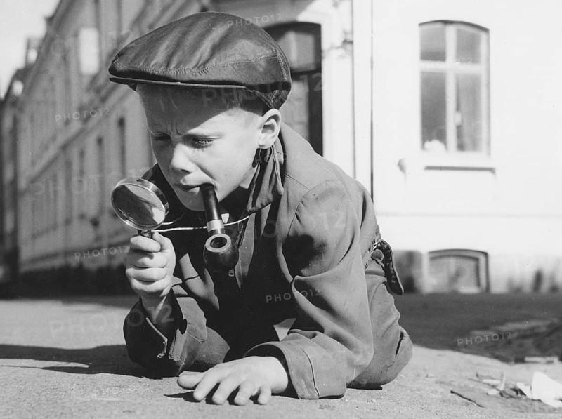 Playing detective. A young boy dressed as a typical looking detective with a magnifying glass and a pipe, is playing outside. Sweden 1961