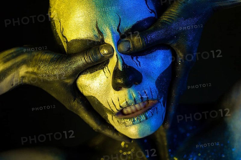 Isolated on black, closeup picture, toned yellow and blue, spooky young blonde caucasian pretty woman with scull body art, closed grey eyes, closes her eyes with her thumbs