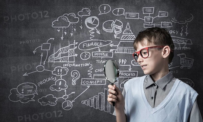 Cute boy looking through magnifying glass against blackboard background