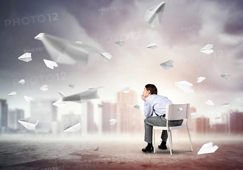 Young businessman sits on an office chair, thoughtful and looking up