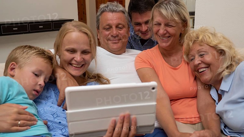 A big family is watching something funny on a pad, close side by side