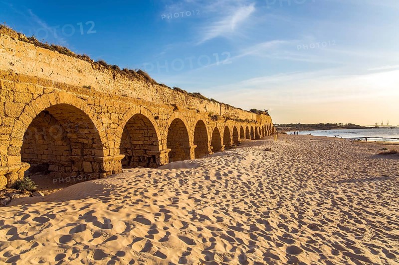 The aqueduct, built in the early Byzantine period. Fantastic sunset on the Mediterranean coast in Caesarea. The sandy beach is trampled by tourists. Concept of active, ecological and historical tourism