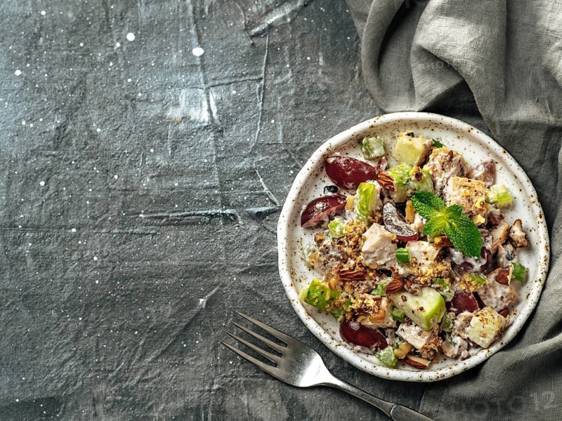 Waldorf salad with copy space. American fruit and nut salad with apples, celery, grapes, chicken meat, dressed mayonnaise. Craft plate with ready-to-eat waldorf salad on gray background. Top view
