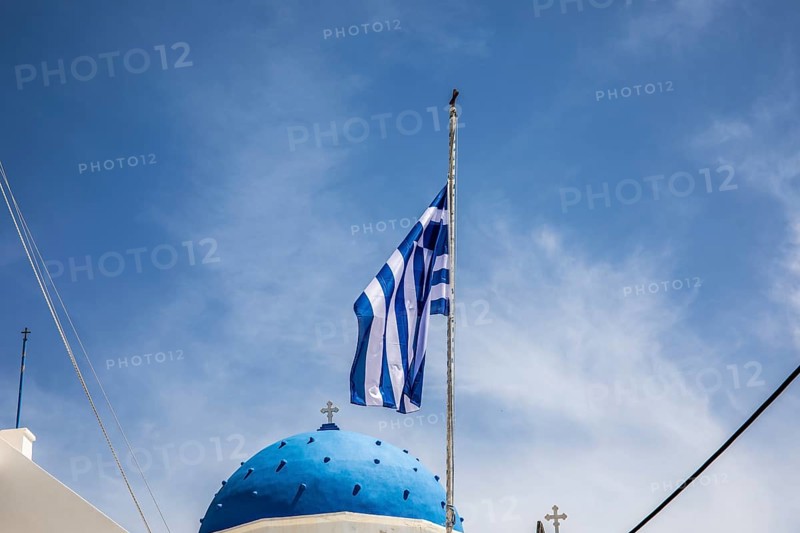 Greek flag waving in the wind, blue church dome, Timios Stavros church, Perissa, Santorini island, Cyclades, Greece