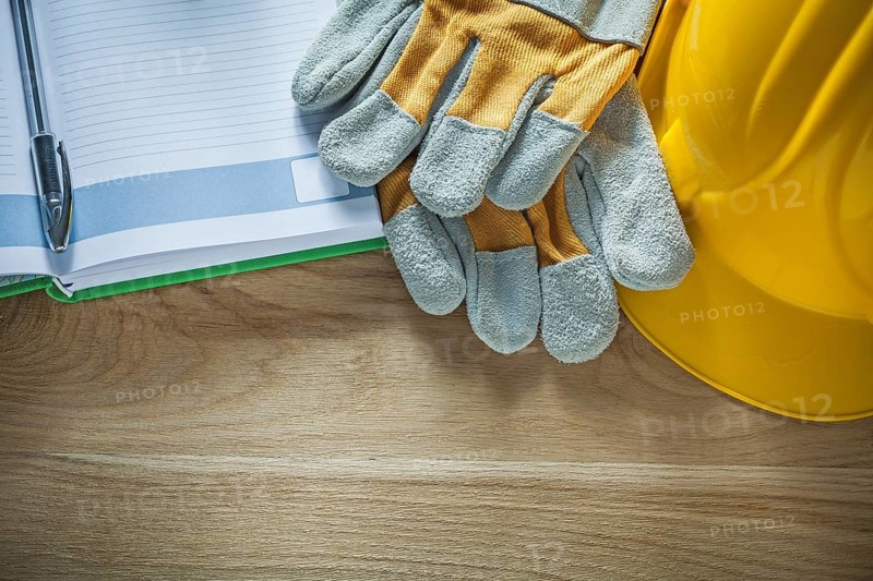 Protective gloves notepad pen safety hard hat on wooden board
