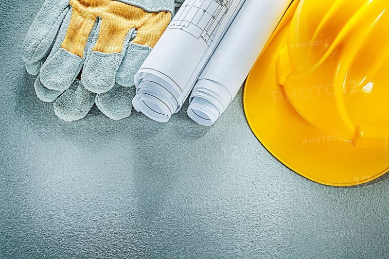 Rolled blueprints hard hat safety gloves on concrete background
