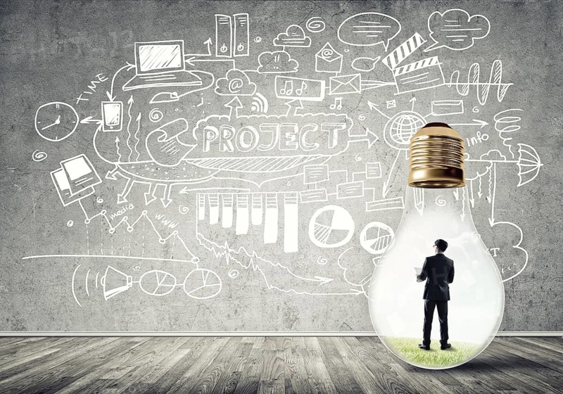Businessman inside of light bulb in empty concrete room and sketches on wall