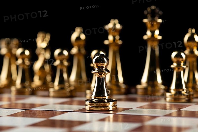 Golden chess figures standing on wooden chessboard. Intellectual duel and tactical battle in business. Strategy planning and leadership concept. Gold metal chess pieces in row on black background