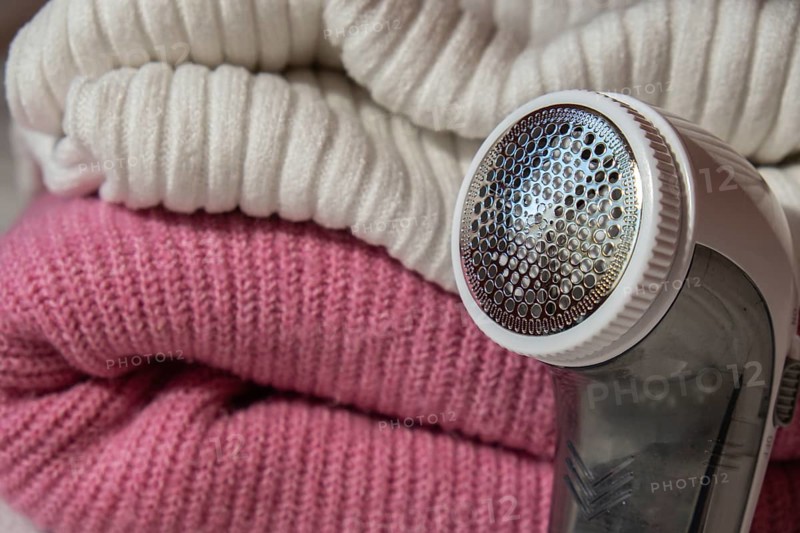 Anti-pilling razor. Device for shaving clothes. Anti-Plush fabric Shaver. Electric portable sweater pill defuzzer Lint remover from pink acrylic or wool sweater. Electric device fabric shaver after cleaning and collected fluff lint. Closeup Pilled sweater. Old used clothes with pilling