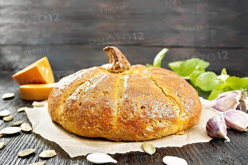 Pumpkin bread on paper, garlic, basil, pieces and seeds of a vegetable on the background of a dark wooden board