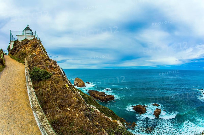 The white building of the lighthouse looks spectacular on a high cape. New Zealand. Nugget Point Lighthouse. Direct path leads to the lighthouse. The concept of active, environmental and photo tourism