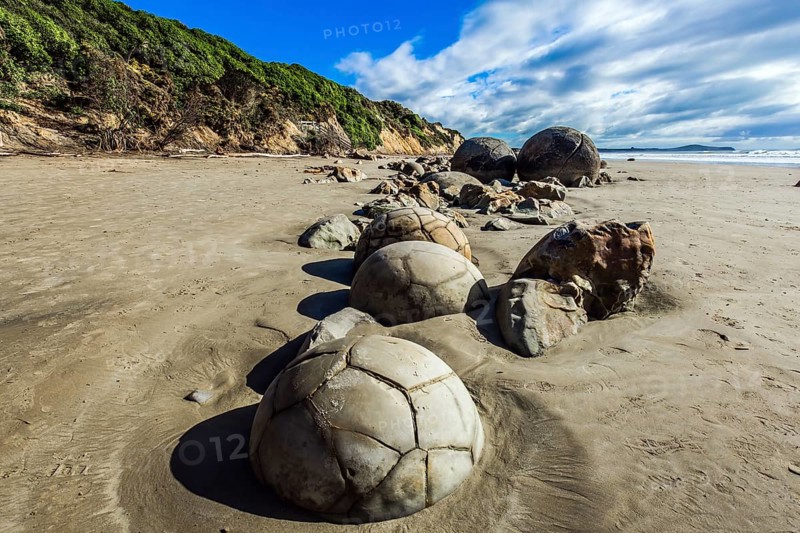 Series of mysterious round boulders Moeraki and their shattered remnants on a sandy beach. New Zealand. Low tide in the Pacific. Popular tourist attraction.The concept of exotic and ecological tourism