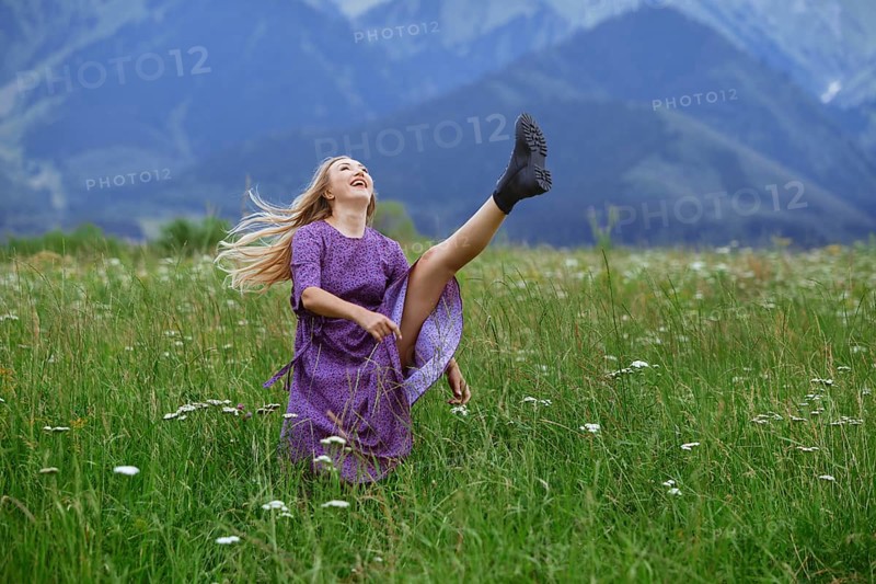 Playful blond woman having fun in the field and raising her leg, USA