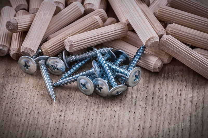 Woodworking dowels and construction nails on wood board top view