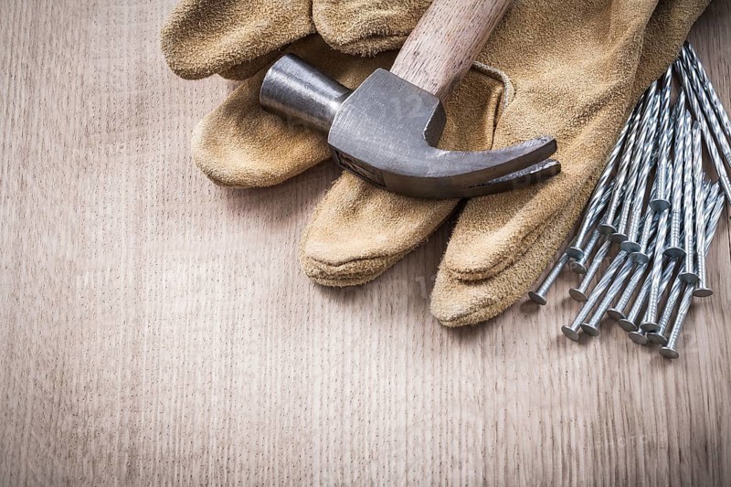 Claw hammer leather protective gloves and heap of metal nails on wooden board close up version construction concept