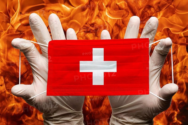 Doctor holding in white gloves protection medical face mask, respiratory bandage with Switzerland national country flag superimposed on mask. Concept on background of dangerous red flames natural fire