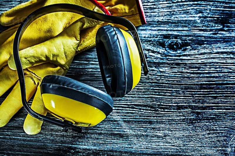 Safety earmuffs leather gloves on wooden board