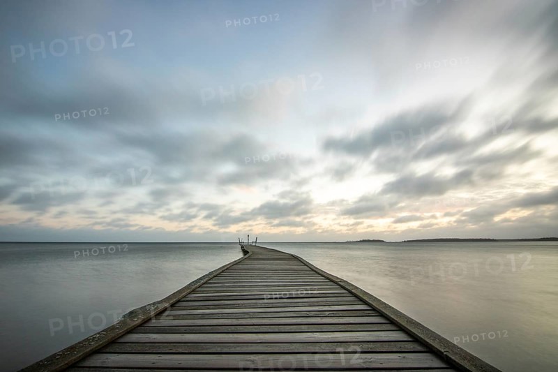 Sunrise over a lake in autumn. A wooden jetty juts into the water, while grass has established itself on the sandy beach. The lake and beach at Lake Vänern in Näs Sannar, Sweden, Scandinavia