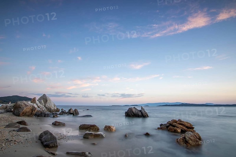 View through rocks on a sandy beach into the sunset. Landscape shot with view to the horizon over the wide sea at the coast of Ouranoupoli, Thessaloniki, Central Macedonia, Greece