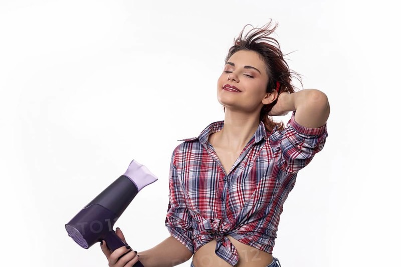 A confidently poised woman happily using a hair dryer, joyfully showcasing beautiful hair styling trends