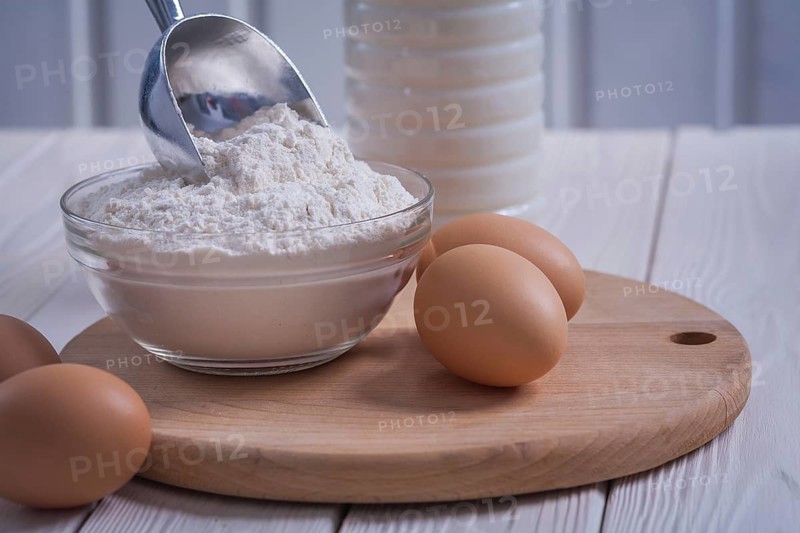 Very close up view eggs flour in bowl scoop bottle of milk on white painted old wooden board food and drink concept