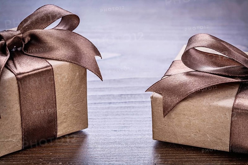 Two vintage pepr giftboxes with brown bows on old wooden board very close up view holiday concept